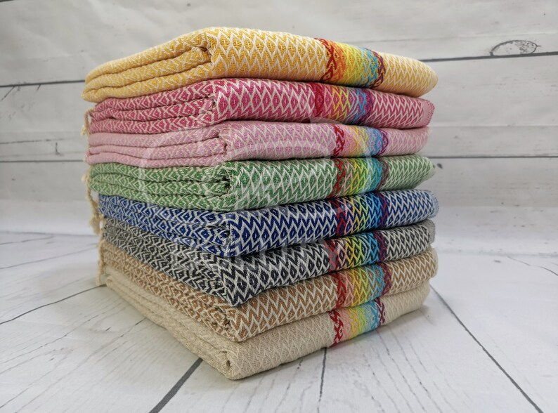 May include: A stack of eight colorful patterned towels with fringed edges. The towels are folded and stacked in a pyramid shape. The towels are made of a soft, absorbent material and are perfect for drying off after a shower or bath.