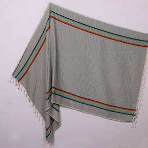 May include: A gray and white patterned beach towel with a rainbow stripe border. The towel has fringe on the edges.