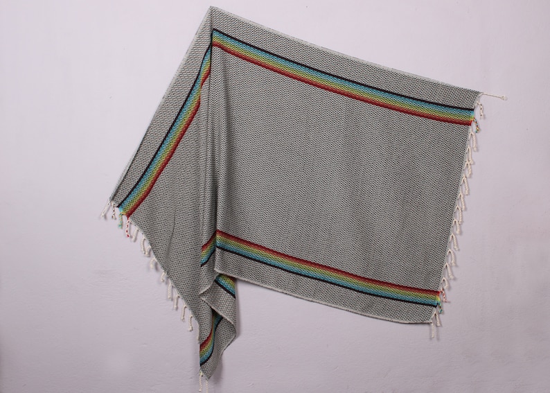 May include: A gray and white patterned beach towel with a rainbow stripe border. The towel has fringe on the edges.