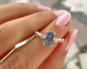 May include: A silver ring with a blue gemstone and smaller clear gemstones. The ring is on a finger.
