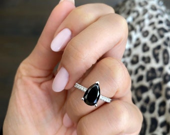 May include: A pear-shaped black diamond engagement ring with a silver band and small diamonds set in the band.