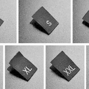 May include: Six black fabric clothing size tags with white text. The tags are labelled XS, S, M, L, XL, and XXL.