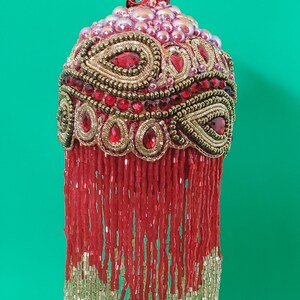 May include: A red and gold beaded Christmas ornament with a fringe of red and gold beads.