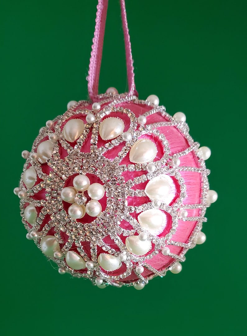 May include: A pink Christmas ornament with a white pearl and rhinestone design