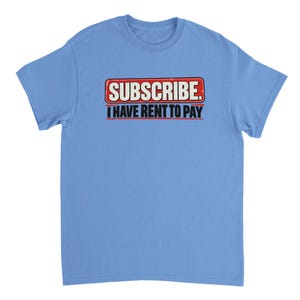 May include: A light blue short-sleeve t-shirt featuring a graphic design with a red rectangular box containing the white text SUBSCRIBE. Below this, the black text I HAVE RENT TO PAY is printed in a bold, sans-serif font on the chest area.