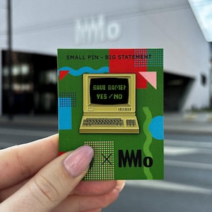 Puede incluir: Pin rectangular con fondo verde que presenta un gráfico de ordenador retro. El texto "SAVE GAME? YES/NO" se muestra en la pantalla. El pin también incluye el texto "SMALL PIN - BIG STATEMENT" y el logotipo "MMo".