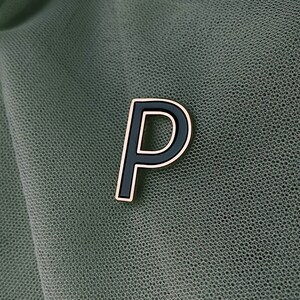 May include: A black letter "P" with a gold outline. The letter is on a green mesh fabric.