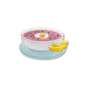 May include: Embroidered patch featuring a bowl of pink soup with a white and yellow egg in the center, green dots, and yellow croutons. The bowl sits on a light blue plate, all against a white background. This patch is perfect for jackets, bags, or other fabric items.