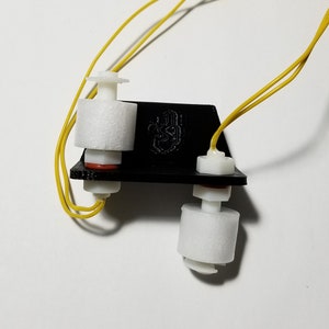 May include: Two white water level sensors with yellow wires attached to a black plastic base. The sensors have a white foam float and a red rubber seal.