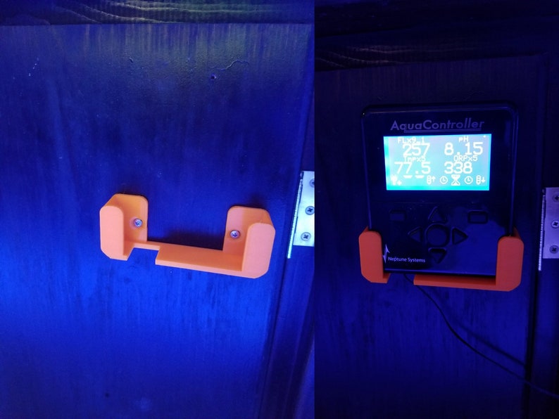 May include: A black AquaController device with an orange 3D printed wall mount. The device has a digital display showing readings for temperature, pH, and salinity. The text "AquaController" is printed on the device.