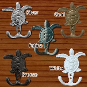 May include: Five cast iron turtle hooks in different finishes: silver, gold, patina, bronze, and white. Each hook has a double hook design and a turtle sculpture on top.