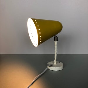 May include: A yellow metal wall lamp with a white base and a flexible arm. The lampshade has a cone shape with small holes.