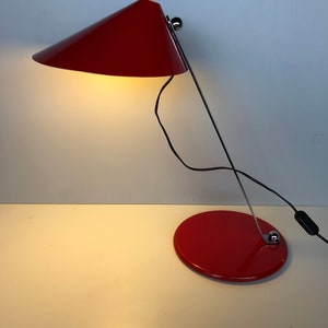 May include: A red desk lamp with a conical shade and a round base. The lamp is made of metal and has a chrome finish.