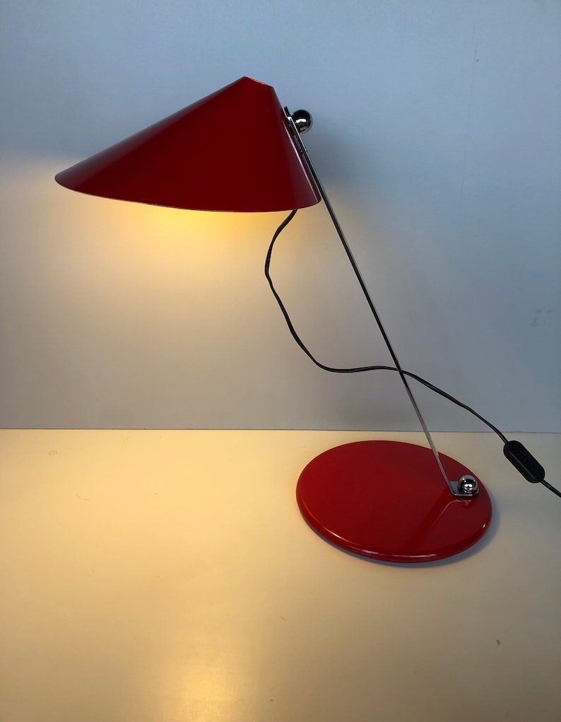 May include: A red desk lamp with a conical shade and a round base. The lamp is made of metal and has a chrome finish.