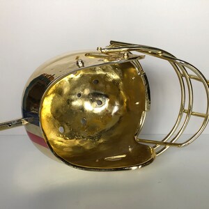 May include: A gold-colored football helmet with a red, white, and blue stripe design. The helmet is open on the top and has a wire face mask.