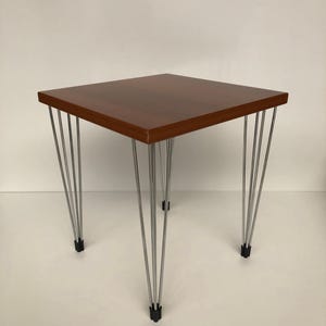 Op de afbeelding: Een kleine, vierkante bijzettafel met een donkerbruin houten blad en chromen haarspeldpoten. De poten zijn schuin en voorzien van zwarte rubberen voetjes. De tafel is ongeveer 46 cm vierkant en 46 cm hoog.