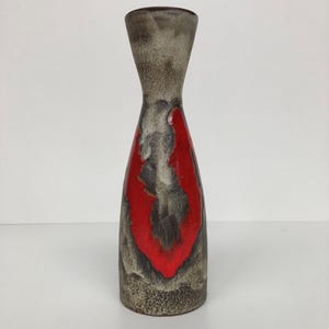 Op de afbeelding: Een hoge keramische vaas met een smalle hals en een bredere basis. Het oppervlak heeft een getextureerde, gevlekte grijs en bruine afwerking met een opvallend, glad, glanzend rood glazuuraccent dat verticaal over het midden loopt.