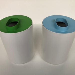 May include: Two modern, cylindrical wastebaskets. One has a green top with an oval opening, the other a light blue top. Both have white bodies. The wastebaskets are made of metal.
