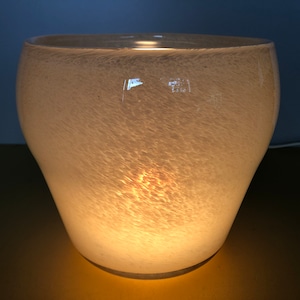 May include: A white glass lamp with a textured surface. The lamp is lit and casting a warm glow.