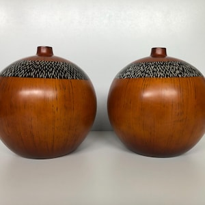 Puede incluir: Dos jarrones de madera con un patrón geométrico marrón y negro. Los jarrones son redondos y tienen un acabado liso y pulido.