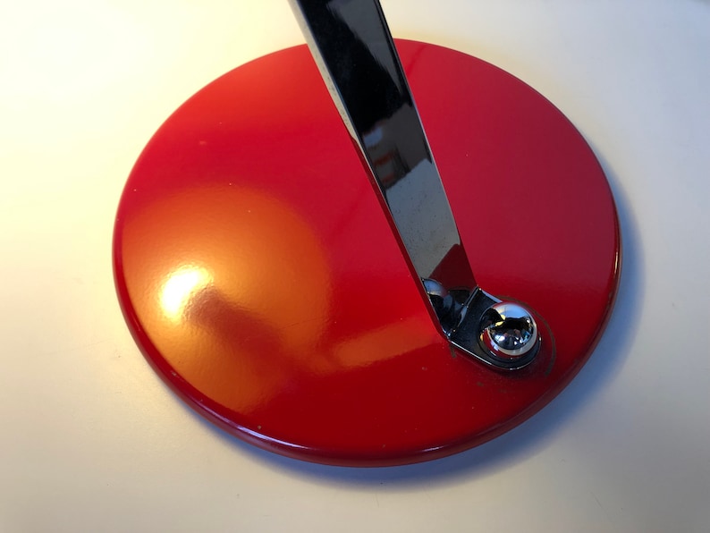 May include: A red circular base with a chrome metal arm attached to it. The base is smooth and shiny.
