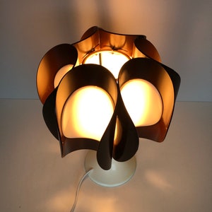 May include: A brown and white table lamp with a unique, flower-shaped design. The lamp has a white base and a brown shade with multiple petals.