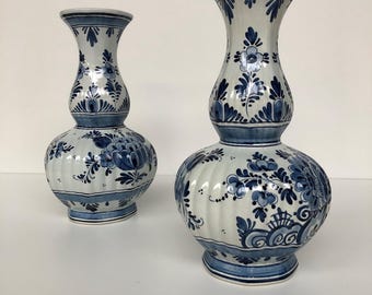 May include: Two ceramic vases with a white and blue floral design. The vases have a bulbous base and a flared top. The larger vase is approximately 12 inches tall, while the smaller one is about 8 inches tall. The vases are decorated with intricate blue floral patterns.