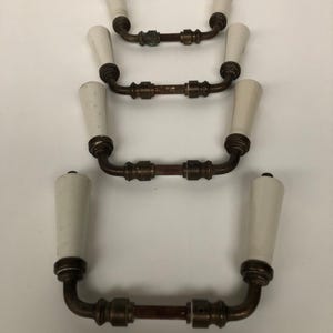 May include: Four antique door handles with white porcelain knobs and bronze metal arms. The handles are arranged in a vertical stack, with the top handle at the top of the image and the bottom handle at the bottom of the image.