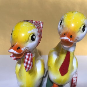 Op de afbeelding: Twee gele eendjes met beschilderde details. Eén eendje draagt een rood-wit geruite sjaal en de andere een rode stropdas.
