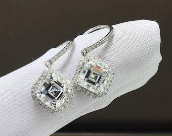 May include: A pair of silver dangle earrings with a square-shaped diamond in the center of each earring. The diamonds are surrounded by a halo of smaller diamonds.