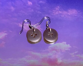 May include: A pair of silver button earrings with a pearl-like finish. The buttons have four holes and are attached to silver hooks.
