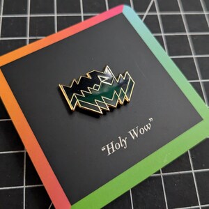 May include: A black and green enamel pin with a geometric design. The pin is on a card with the text "Holy Wow".