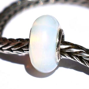 May include: A smooth, oval-shaped white opal bead with a subtle iridescent sheen, mounted on a thick, braided sterling silver chain. The bead features a polished, translucent surface that reflects light, centered on the dark, textured metal link chain.