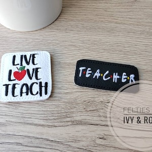 May include: Two felt patches with embroidered text. The white patch says "Live Love Teach" with a red apple in the middle. The black patch says "TEACHER" with colorful dots between the letters.