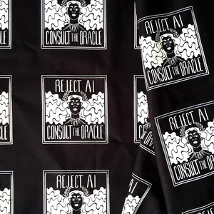 May include: Black fabric featuring a repeating white graphic print of a person with wavy hair wearing a laurel wreath. The text REJECT AI CONSULT THE ORACLE is printed in a rectangular frame around the figure, creating a consistent pattern.