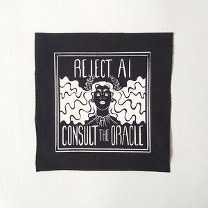 May include: A square black fabric patch featuring a white screen-printed graphic of a figure with long wavy hair wearing a laurel wreath. The text REJECT AI is printed above the figure and CONSULT THE ORACLE is printed below, all within a border.