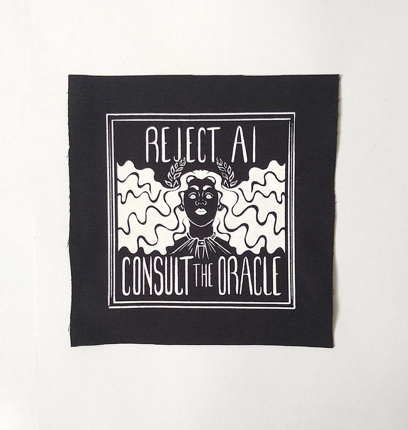 May include: A square black fabric patch featuring a white screen-printed graphic of a figure with long wavy hair wearing a laurel wreath. The text REJECT AI is printed above the figure and CONSULT THE ORACLE is printed below, all within a border.