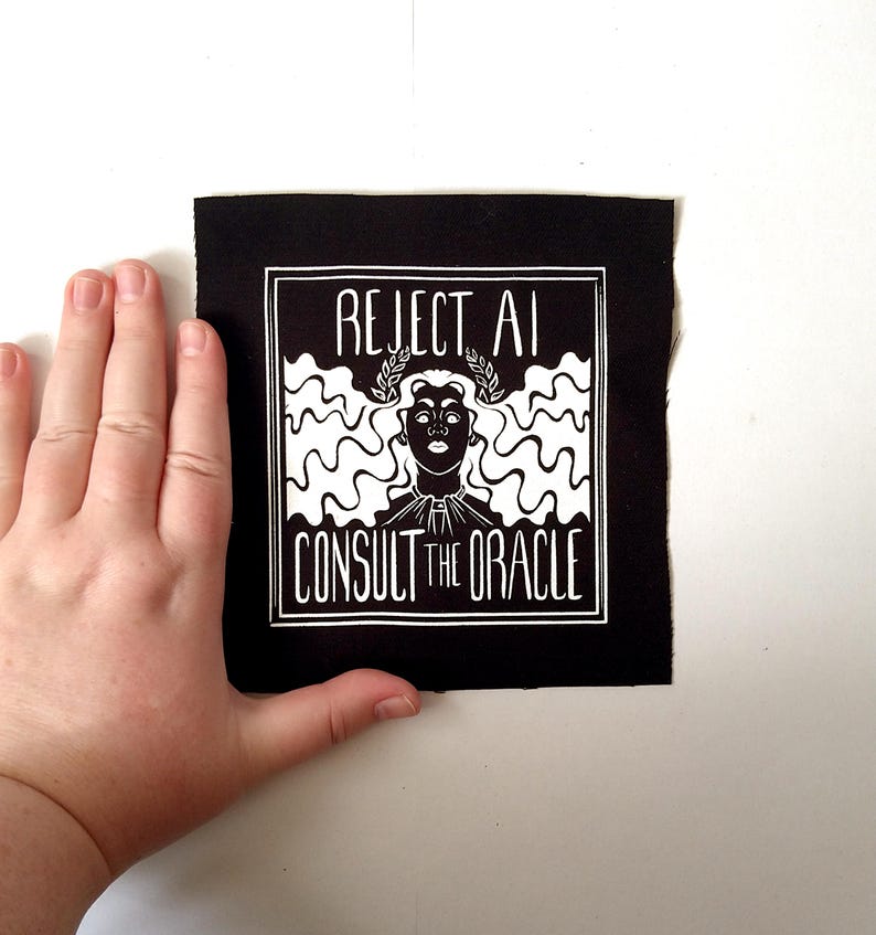 May include: A square black fabric patch featuring a white screen-printed graphic of a person with long wavy hair wearing a laurel wreath. The text REJECT AI is printed above the head and CONSULT THE ORACLE is printed below the graphic design.