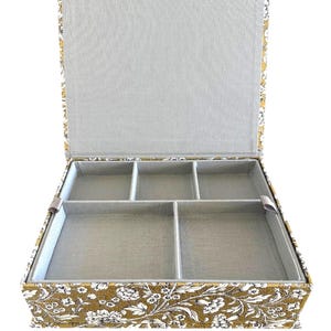May include: A rectangular storage box with an open lid, featuring a mustard yellow exterior with a white floral pattern. The interior is lined with light gray fabric and divided into five separate compartments of varying sizes for organization.