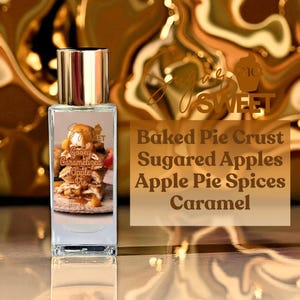 May include: A rectangular perfume bottle with a gold cap. The label features a picture of apple pie and the words "Gooey Caramelized Apple Pie." Text on the right reads "Baked Pie Crust, Sugared Apples, Apple Pie Spices, Caramel."
