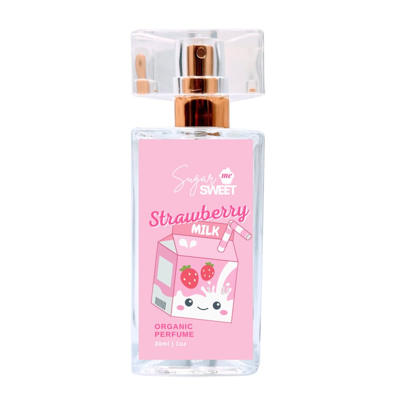 May include: A clear glass perfume bottle with a pink label featuring the words "Sugar me SWEET" and "Strawberry MILK". The label also has a cartoon illustration of a strawberry milk carton. The bottle has a gold-colored sprayer and a clear plastic cap. The bottle contains 1 oz of organic perfume.