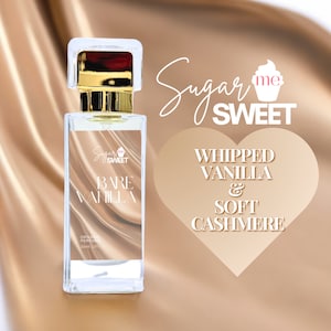 May include: A clear glass perfume bottle with a gold cap and the words "Bare Vanilla" on the label. The bottle is set against a backdrop of a satin fabric and a heart-shaped graphic that reads "Whipped Vanilla & Soft Cashmere."