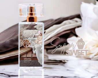 May include: A rectangular perfume bottle with a clear cap and gold-colored accents. The label reads "Cashmere Cream" and "Organic Perfume 30ml | 1oz." The background features soft fabrics and the words "Sugar me Sweet."
