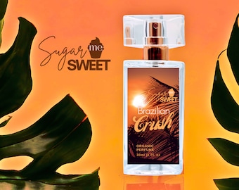 May include: A clear rectangular perfume bottle with a gold-colored atomizer and a label featuring a sunset scene and the words "Brazilian Crush." The bottle is labeled "Organic Perfume" and contains 1 fl oz (30ml). The brand logo "Sugar Me Sweet" is also visible.