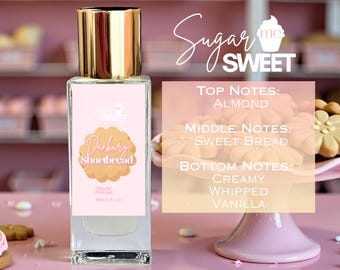 Puede incluir: Un frasco de perfume con tapa dorada y una etiqueta rosa con el texto "Danbury Shortbread". La etiqueta también enumera las notas de salida, corazón y fondo: almendra, pan dulce, vainilla batida cremosa. El frasco es de 30 ml (1 fl oz).