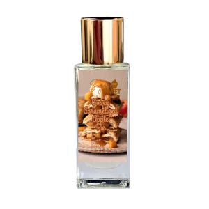 May include: A rectangular perfume bottle with a gold cap. The label features a stack of apple pie with ice cream and the words "Sugar Sweet" and "Gooey Caramelized Apple Pie". The bottle is clear, allowing the liquid inside to be visible.