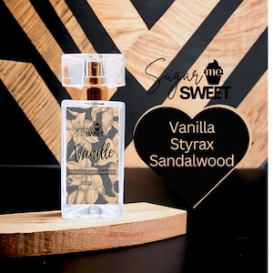 May include: A clear rectangular perfume bottle with a gold-colored cap and a clear lid. The label reads "Vanille" with "Sugar Me Sweet" branding and floral design. The scent notes are Vanilla, Styrax, and Sandalwood.
