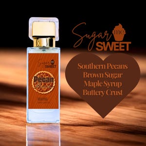 May include: A rectangular perfume bottle with a gold cap and a brown label featuring the text "Pecan Pie" and "Sugar Me Sweet." The label also lists "Organic Perfume" and the volume. A heart-shaped graphic lists ingredients: Southern Pecans, Brown Sugar, Maple Syrup, and Buttery Crust.