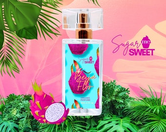 May include: A clear perfume bottle with a gold-colored top and a light blue label featuring a dragon fruit design. The bottle is labeled "Beija Flor" and "Organic Perfume". The background is pink with green tropical leaves.