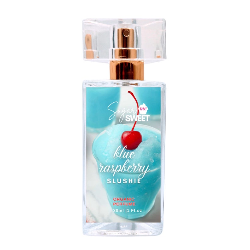 May include: A clear perfume bottle with a gold-colored atomizer and a transparent cap. The label features a blue slushie with a red cherry and the text "Sugar me SWEET blue raspberry SLUSHIE ORGANIC PERFUME 30ml | 1 Fl.oz."